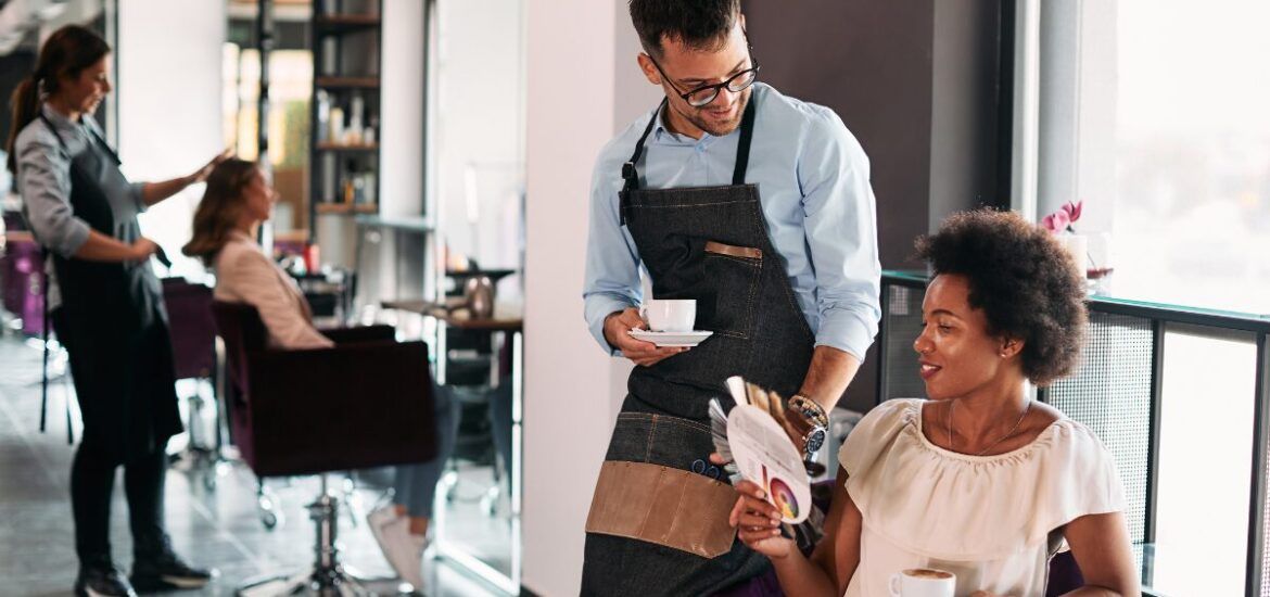 Male hairstylist and his African American female client talking about hair colors while drinking coffee at the salon