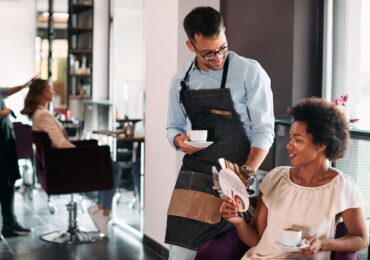 Male hairstylist and his African American female client talking about hair colors while drinking coffee at the salon