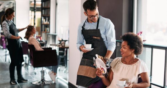 Male hairstylist and his African American female client talking about hair colors while drinking coffee at the salon