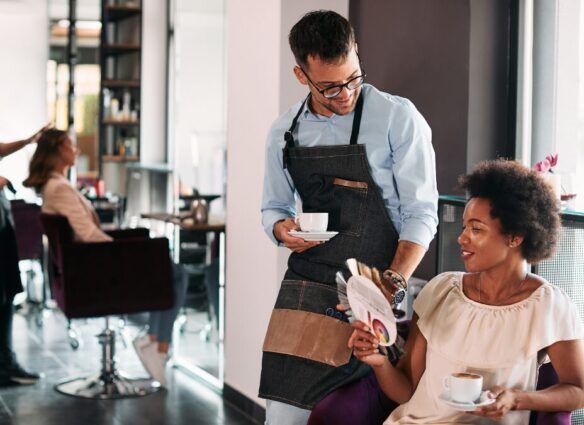 Male hairstylist and his African American female client talking about hair colors while drinking coffee at the salon