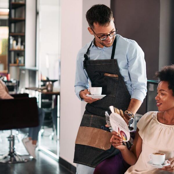 Male hairstylist and his African American female client talking about hair colors while drinking coffee at the salon
