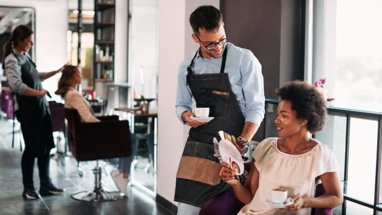 Male hairstylist and his African American female client talking about hair colors while drinking coffee at the salon