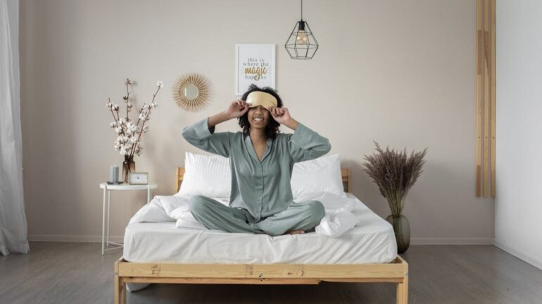woman with eye mask sitting in bed smiling