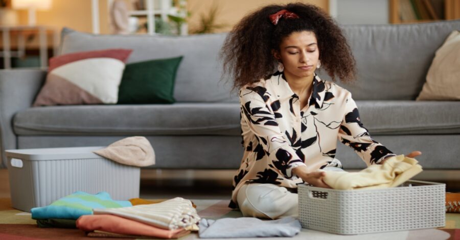 Portrait of young African American woman folding and putting away clean clothes while cleaning home on weekend