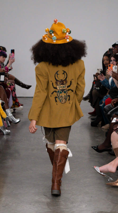 The NYFW model walking backwards showcasing "DYKE" written on the back of their blazer beaded over a bug figure.