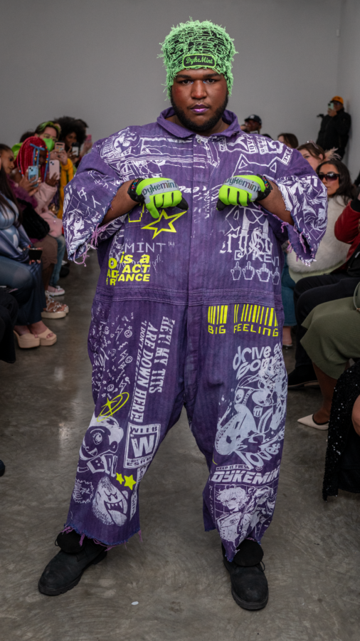 NYFW Model is posed in a purple jumpsuit with drawings all over and green gloves.