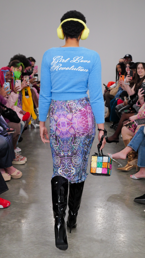 The NYFW model walking backwards showcasing "Girl Love Revolution" written on the back of their cardigan.