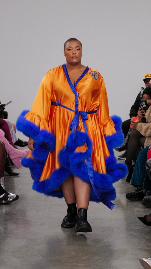 NYFW Model is walking in an orange robe that has blue fur trim.