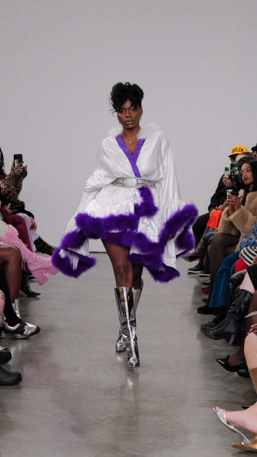 NYFW Model is walking in a white robe that has purple fur trim.