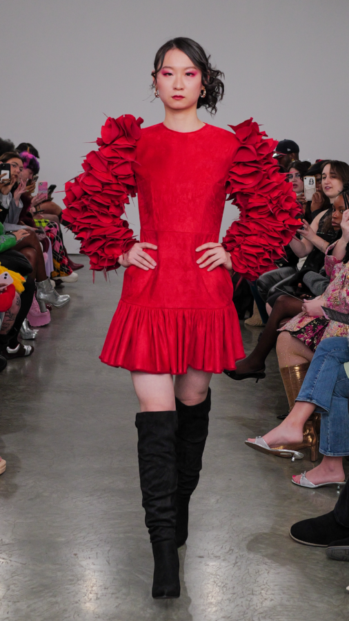 NYFW Model is wearing a red dress with dramatic sleeves resembling rose petals. The model has on closed toe thigh-high boots.