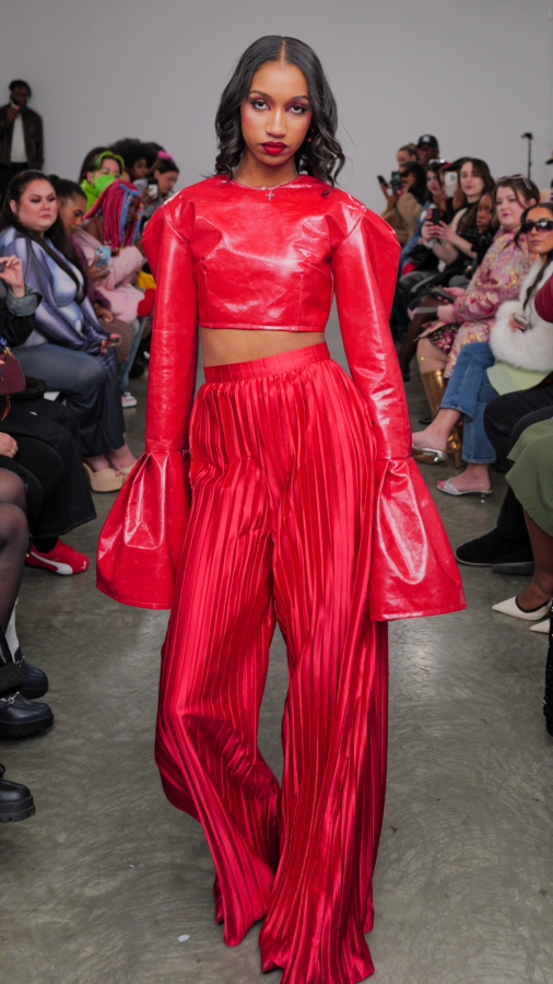 The NYFW model is wearing a red long sleeve crop top with coordinating high waist paints.